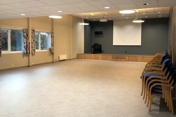 Stor sal med scene, prosjektorlerret og god gulvplass.